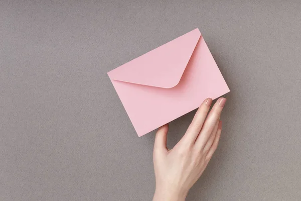 Envelope rosa em mulheres mão sobre o fundo cinza. Conceito de correio — Fotografia de Stock