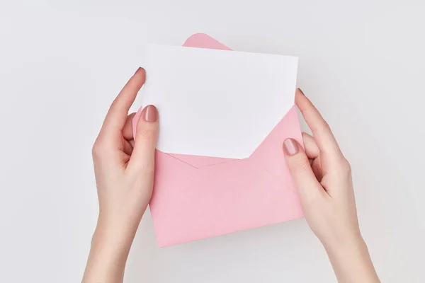 Envelope rosa com cartão postal branco em branco nas mãos das mulheres sobre o fundo branco. Conceito de correio — Fotografia de Stock