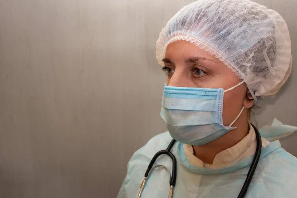 Doktor ya da hemşire üniformalı, maskeli, şapkalı ve steteskoplu. Beyaz kadın portresi, fotokopi aletiyle ışık desenli arka planda yarım yüz pozisyonu alarak kameraya bakmıyor.