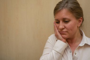 Orta yaşlı kadın portresi elleriyle yüzüne dokunuyor. 40 yıllık kadın kameraya bakmıyor. Beyaz iş gömleği giyindi. Üzgün yüz ve olumsuz duygular