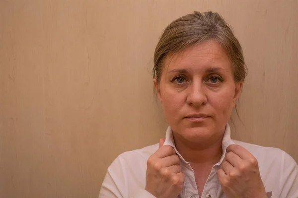 Beyaz iş gömleğinin yakasına dokunan orta yaşlı kadın portresi. 40 yaşında beyaz bir kadın kameraya bakıyor ve gülümsemiyor. Sakin bir yüz ve duygusuz. Kopyalama alanı olan arkaplan
