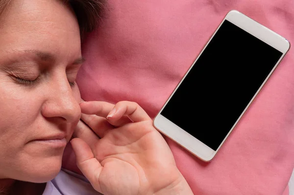 女人睡在床上带着手机 40岁的中年妇女躺在枕头和智能手机上 旁边有黑屏 社交网络或网瘾 — 图库照片
