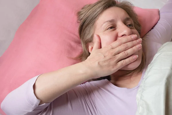 女人醒来 打呵欠 40岁妇女的特写 她面容平静 躺在粉色枕头和白色被褥上 快乐早晨的概念 — 图库照片