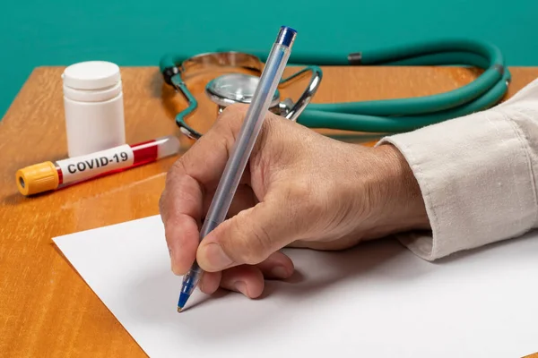 Muayenehane formunu dolduran bir doktorun eli. Covid-19 şüphesi olan bir hasta için.