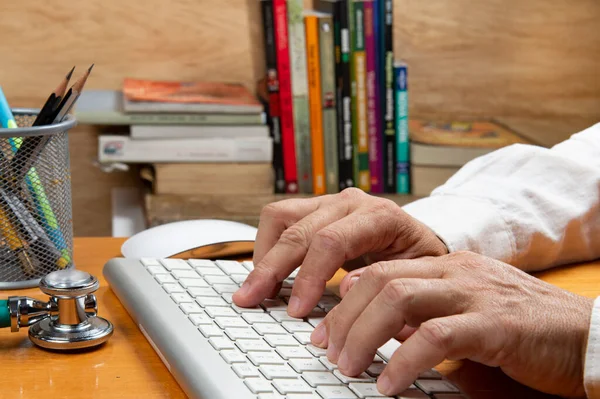 Person with hand on keyboard at an office desk with a stethoscope, pencil holder and books in the background