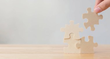 Hand of male or female putting jigsaw puzzle connecting on wooden desk and wall background, Strategic management and business solutions for success