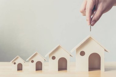 Property investment and house mortgage financial concept, Hand putting money coin in wooden houses arranged different size in row