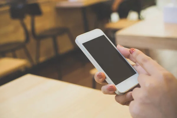 Primer plano de la mano de la mujer utilizando el teléfono inteligente en la mesa de madera en el restaurante, Plantilla dispositivo de pantalla negra teléfono móvil — Foto de Stock