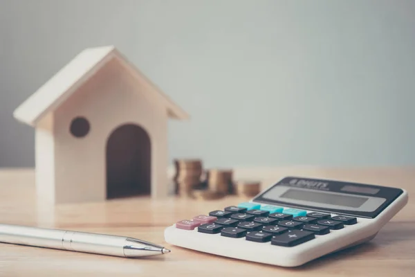 Calcolatrice con casa in legno e monete pila e penna su tavolo in legno. Investimento immobiliare e ipoteca casa concetto finanziario — Foto Stock