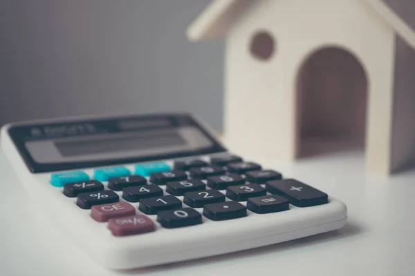 Kalkulačka s dřevěným domem na bílém stole. Investice do nemovitostí a hypoteční finanční koncept — Stock fotografie