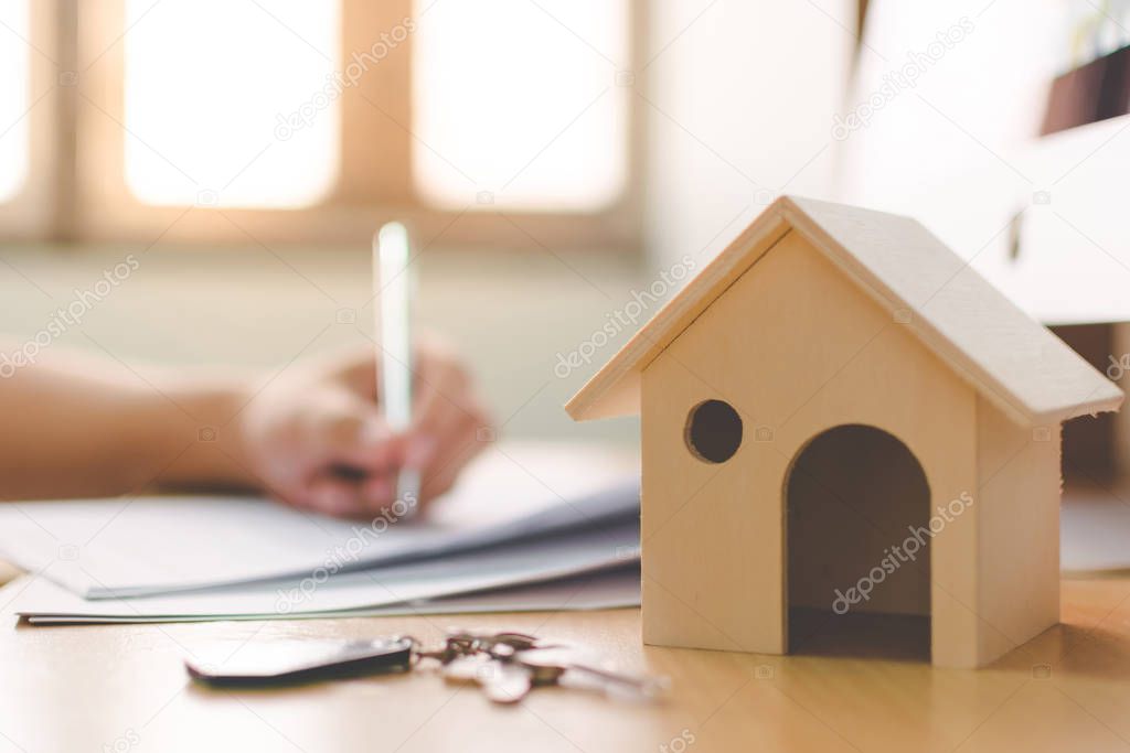 Wooden home model and key house on wood table with hand signing the document contract loan or mortgage property investment