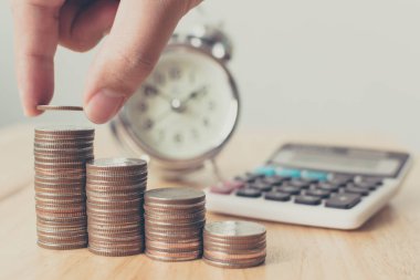 Yatırım konsepti için para biriktiren erkek ya da kadın eli madeni para yığını koyuyor. Hesap makinesi ve saatle büyüyen finansal büyüme.