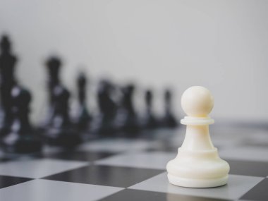 Stratejik planlama iş rekabeti konsepti. Satranç tahtasında siyah satranç taşlarıyla çevrili beyaz piyon.