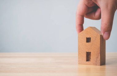 Emlak yatırımı gayrimenkul ve ev ipoteği finansal konsepti. Elle tutulan ahşap ev masanın üstünde.