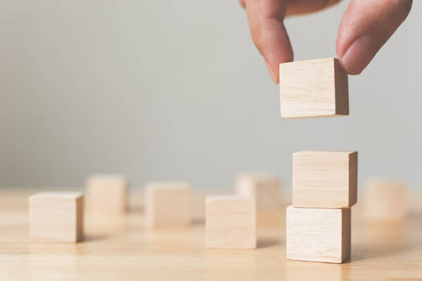 Hand arranging wood block stacking on top with wooden table. Business concept for growth success process. Copy space