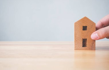 Emlak yatırımı gayrimenkul ve ev ipoteği finansal konsepti. Elle tutulan ahşap ev masanın üstünde.