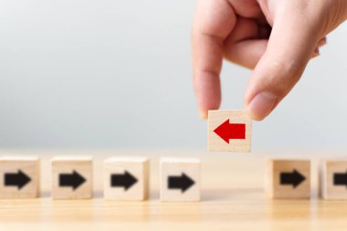 El ele tutuşan ahşap blok ve kırmızı ok ters yöne bakan siyah oklar, Eşsiz, farklı düşün, bireysel ve kalabalığın konseptinden uzak dur