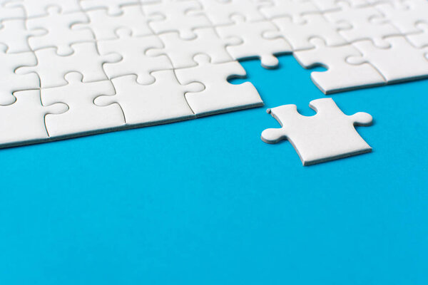 White jigsaw puzzle on blue background. Team business success partnership or teamwork.