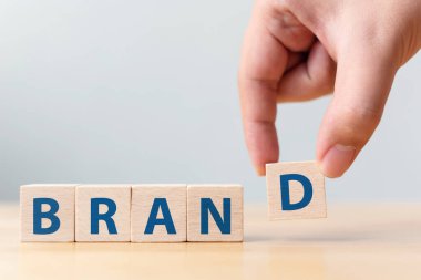 Erkek eli tahta masaya Brand sözcüğüyle tahta küp bloğu koyuyor. Başarı için marka oluşturma