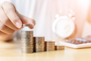 Konsept, para tasarrufu, finansal iş yatırımları. Bozuk para yığını koyan erkeğin eli saat ve hesap makinesiyle artan büyüme değeri