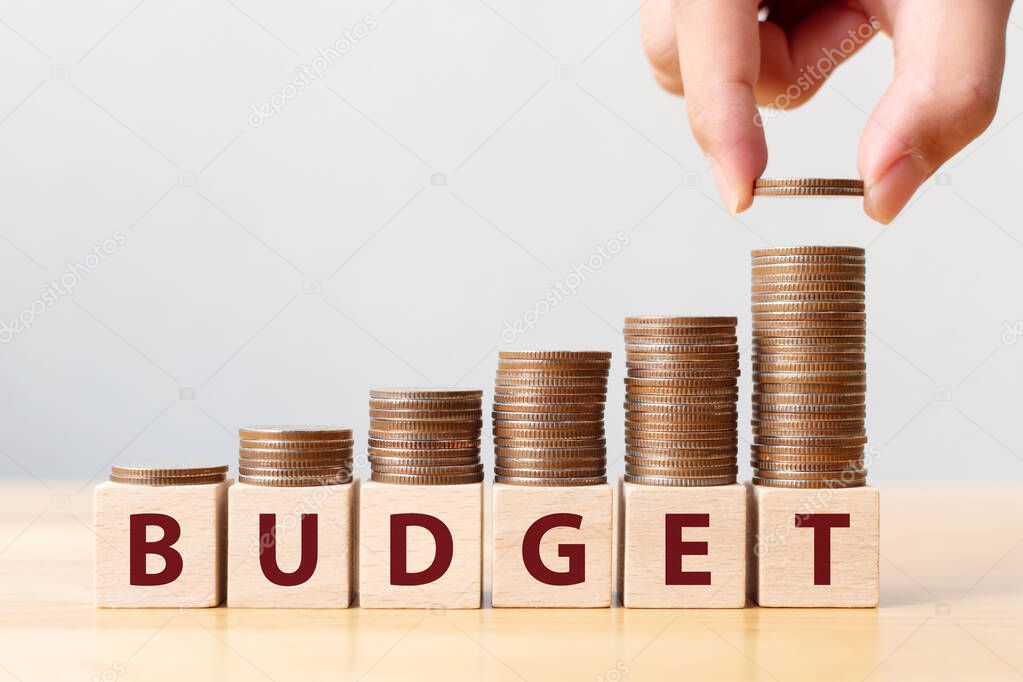 Hand putting coins on stack stair as step growing growth and wooden cube block with word BUDGET. Money annual budget concept
