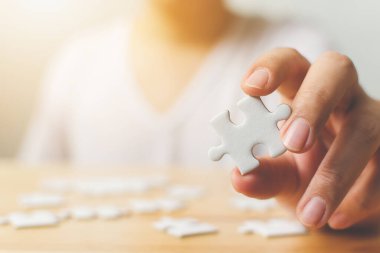 Tahta masadaki beyaz yapboz parçalarını birleştirmeye çalışan bir erkek eli. Alzheimer hastalığı, bunama, hafıza kaybı, otizm farkındalığı ve akıl sağlığı konsepti için sağlık hizmetleri
