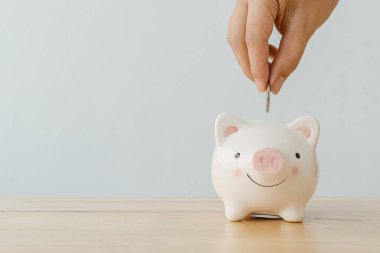 Para tasarrufu konsepti finansal iş yatırımları. Domuz kumbarasına ahşap masanın üzerine bozuk para koyan bir adamın eli.