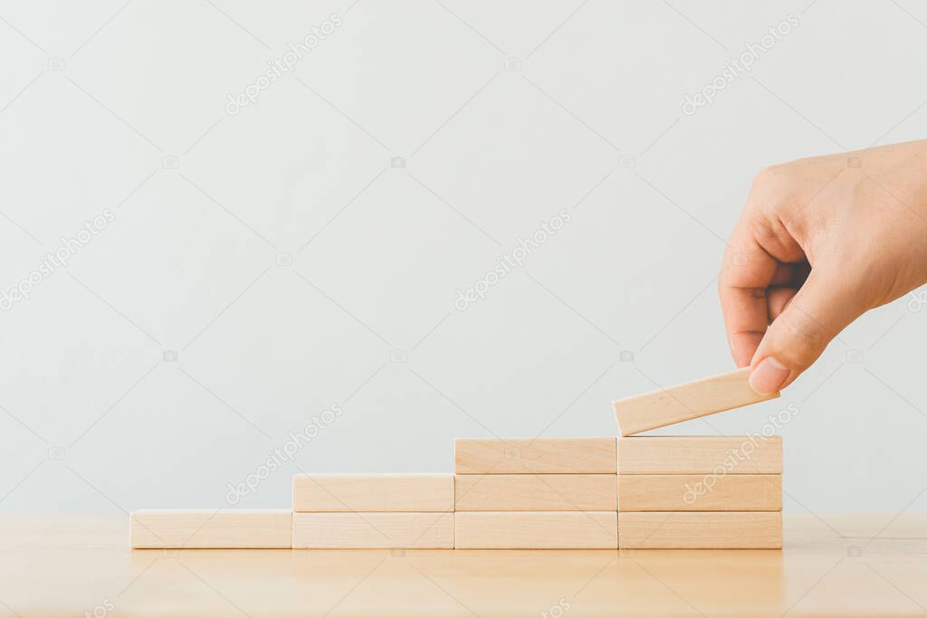 Hand arranging wood block stacking as step stair. Ladder career path concept for business growth success process