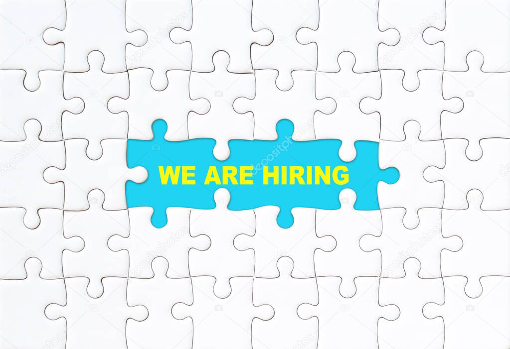We are hiring concept. White jigsaw puzzle with word and blue background