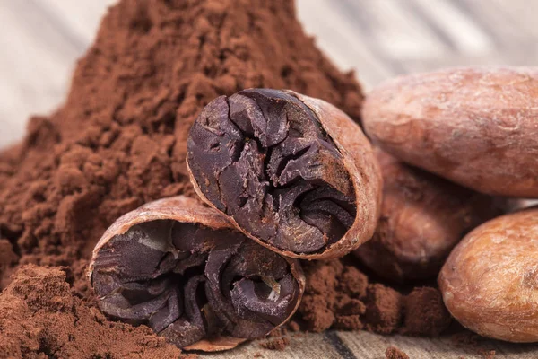 Cocoa beans and powder on wooden plank. — Stock Photo, Image