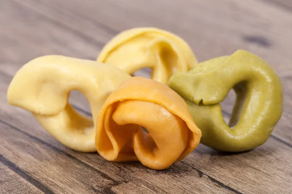 Gekleurde tortellini, ringvormige pasta op houten plank — Stockfoto