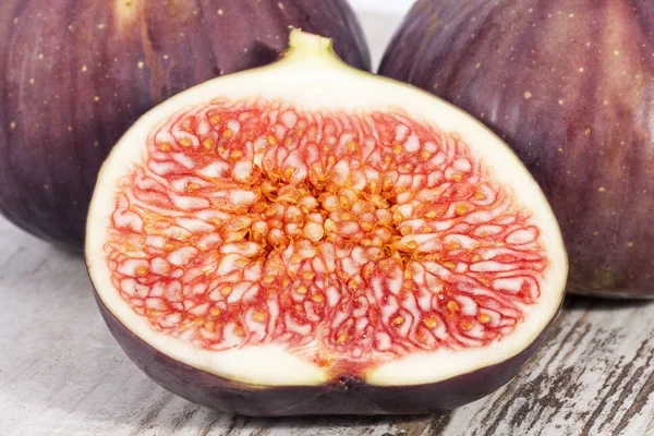 Fruits of whole and half fresh figs on wooden plank, close up. — Stock Photo, Image