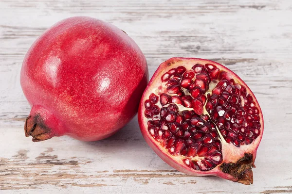 Fruits of red pomegranate, whole and sectioned, on wooden plank — Stock Photo, Image