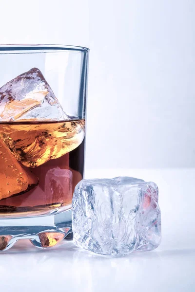 Whiskey glass with ice cubes on white glass surface over white background