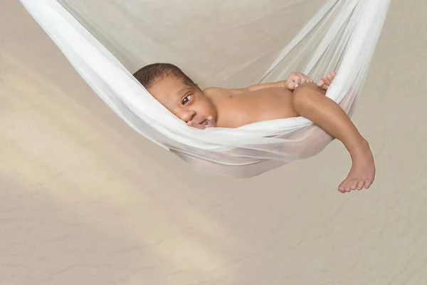 婴儿三周大男孩放松在一个明确的白色 see-through 吊床挂微笑偷看看着相机使眼睛接触不睡觉不穿衣服混合种族加勒比 — 图库照片