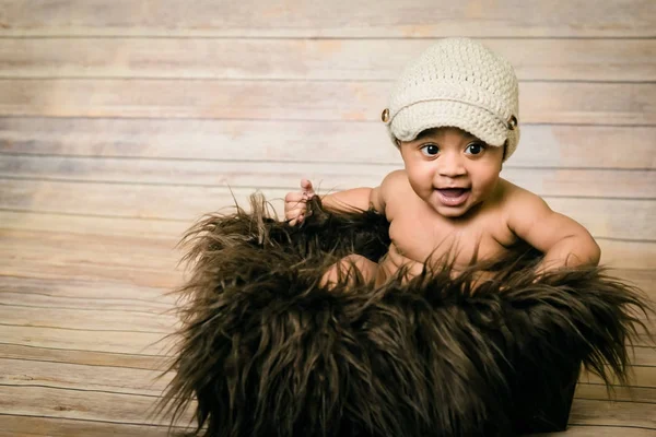 婴儿混合种族健康寻找男婴穿着针织帽坐在蓬松的毛茸茸的篮子木背景的现代工作室拍摄复古看起来微笑快乐六月老有乐趣 — 图库照片