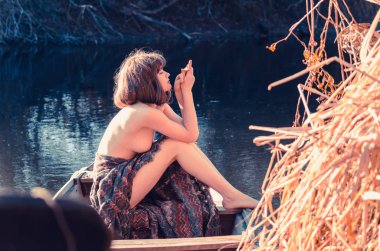 Gün batımında teknede genç seksi kadın. Kız çiçek çelenk kafasında, rahatlatıcı ve Nehri üzerinde yelken vardır. Güzel vücut ve yüz. Fantezi sanat fotoğraf. Kavramı içinde kadın güzelliği, dinlenme