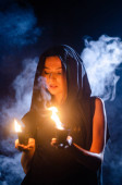 záhadná mladá dívka v černém plášti, čarodějnická sabat v lese v noci u ohně