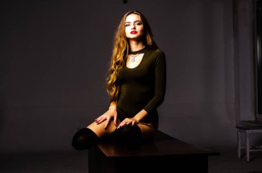 Güzel dansçı. Kız model. Kız bir şapkanın içinde oturuyor ve masaya oturuyor. Güzel iç çamaşırlı bir kız. Kız masada oturuyor ve maskaralık yapıyor, surat asıyor. pürüzsüz, bakımlı bacaklar.