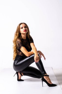 deri kıyafet giyen siyah saçlı kız tam uzunlukta portre. bir silah tutarken oturmuş poz, beyaz bir stüdyo arka plan üzerinde izole.