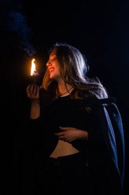 Gizemli genç kız siyah pelerin giyiyor, cadıların Şenlik ateşinin yanındaki ormanda Şabat günü