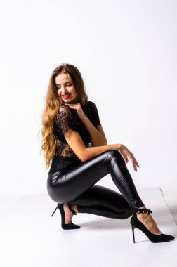 deri kıyafet giyen siyah saçlı kız tam uzunlukta portre. bir silah tutarken oturmuş poz, beyaz bir stüdyo arka plan üzerinde izole.