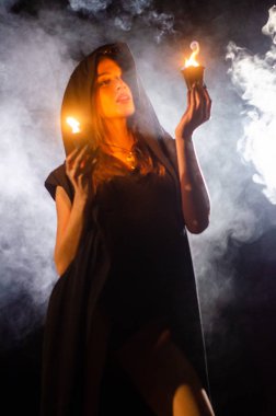 Gizemli genç kız siyah pelerin giyiyor, cadıların Şenlik ateşinin yanındaki ormanda Şabat günü