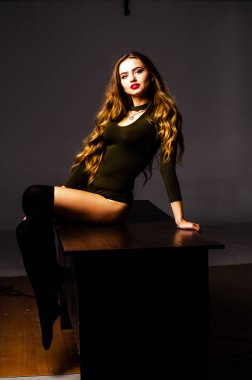 Güzel dansçı. Kız model. Kız bir şapkanın içinde oturuyor ve masaya oturuyor. Güzel iç çamaşırlı bir kız. Kız masada oturuyor ve maskaralık yapıyor, surat asıyor. pürüzsüz, bakımlı bacaklar.