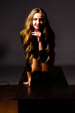 Güzel dansçı. Kız model. Kız bir şapkanın içinde oturuyor ve masaya oturuyor. Güzel iç çamaşırlı bir kız. Kız masada oturuyor ve maskaralık yapıyor, surat asıyor. pürüzsüz, bakımlı bacaklar.