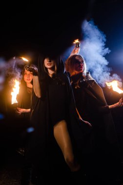 Siyah pelerinli gizemli genç kızlar, Şenlik ateşinin yanındaki ormanda cadı ayini.