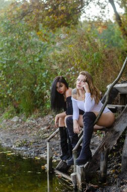 Nehir kenarında poz veren siyah ve beyaz elbiseli iki seksi genç kız.