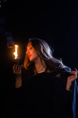 Gizemli genç kız siyah pelerin giyiyor, cadıların Şenlik ateşinin yanındaki ormanda Şabat günü
