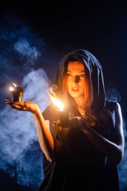 Gizemli genç kız siyah pelerin giyiyor, cadıların Şenlik ateşinin yanındaki ormanda Şabat günü