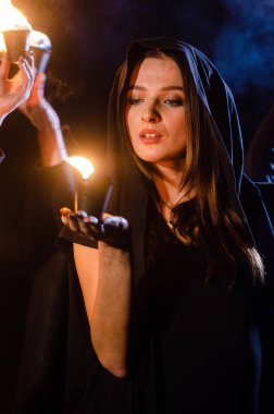 Gizemli genç kız siyah pelerin giyiyor, cadıların Şenlik ateşinin yanındaki ormanda Şabat günü